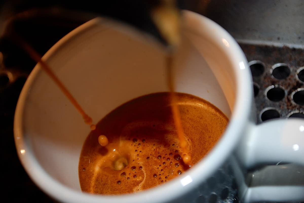 Two streams of espresso pouring from a double spout into a white cup