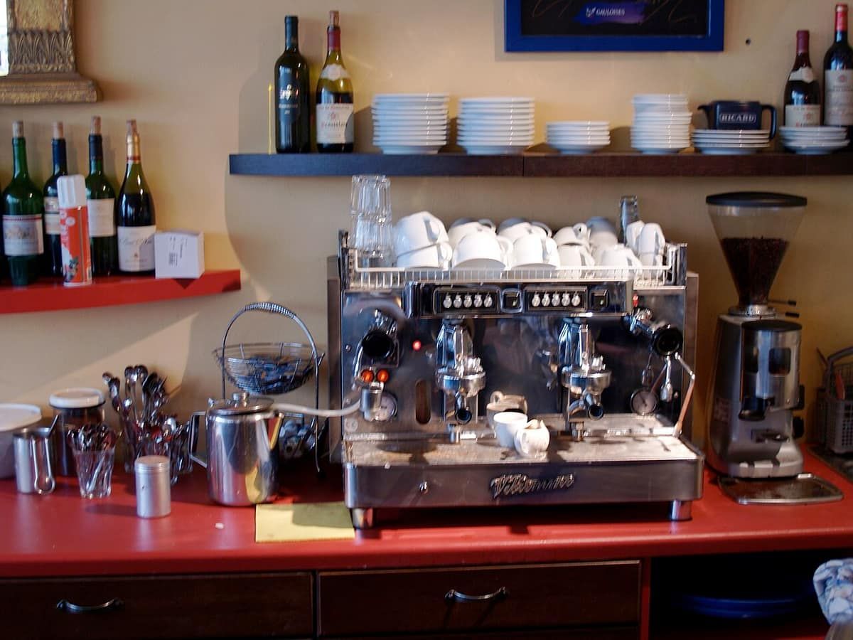 A chrome espresso machine and grinder on a café counter with cups stacked on top
