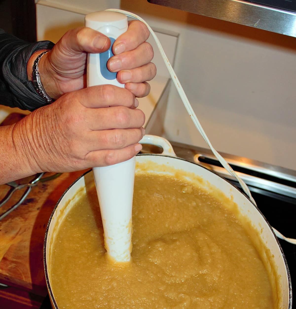 A hand holding an immersion blender in a pot of puréed applesauce