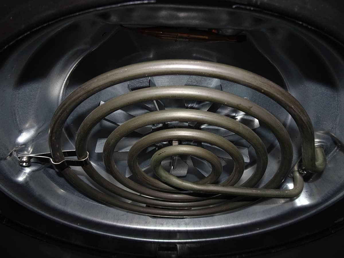 Close-up of an air fryer's coiled heating element and the fan guard behind it