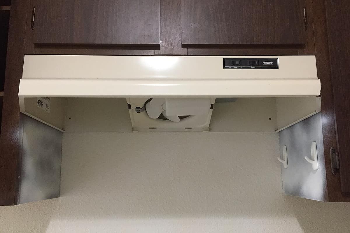 The underside of a cream-colored range hood mounted below kitchen cabinets