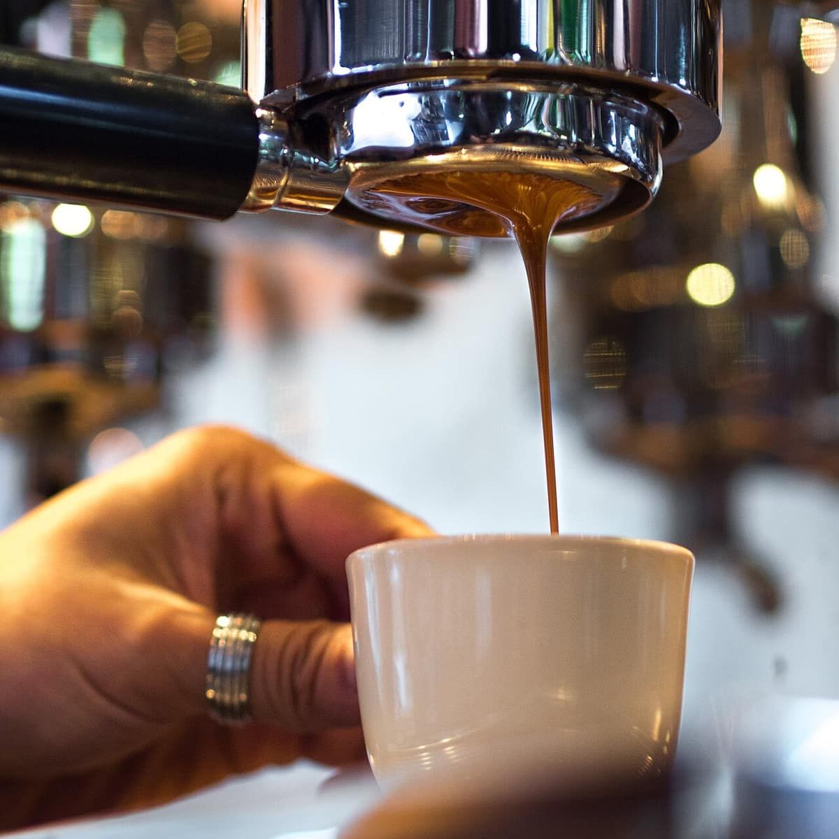 Espresso streaming from the bottom of a bottomless portafilter into a white cup