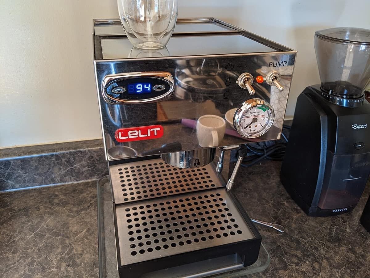 A stainless home espresso machine with a pressure gauge and a portafilter, next to a coffee grinder