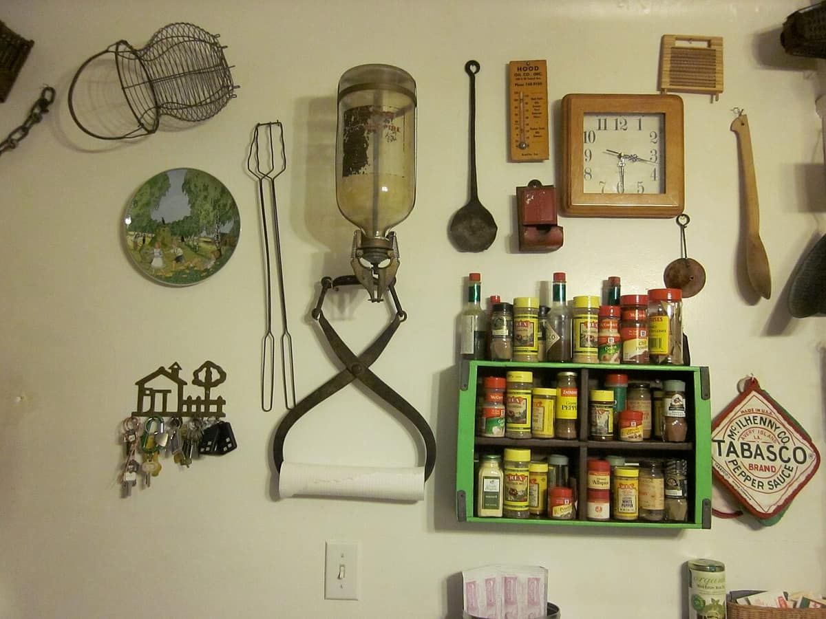 An old-style fire extinguisher mounted on a home kitchen wall next to a spice rack and a clock