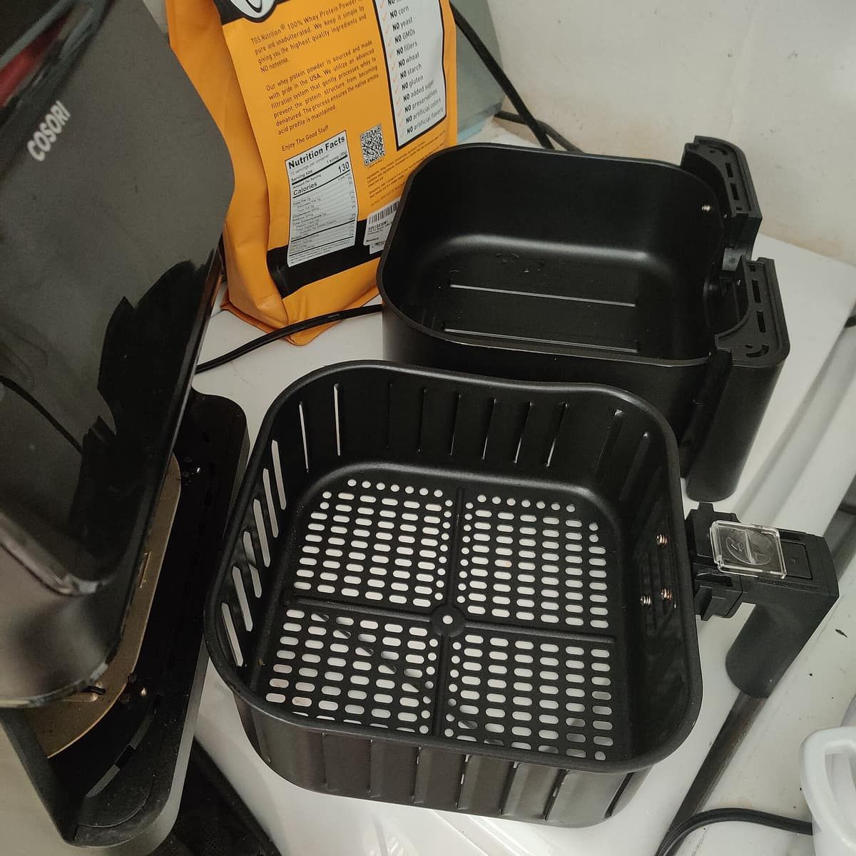 An air fryer basket and its perforated crisper tray removed from the unit