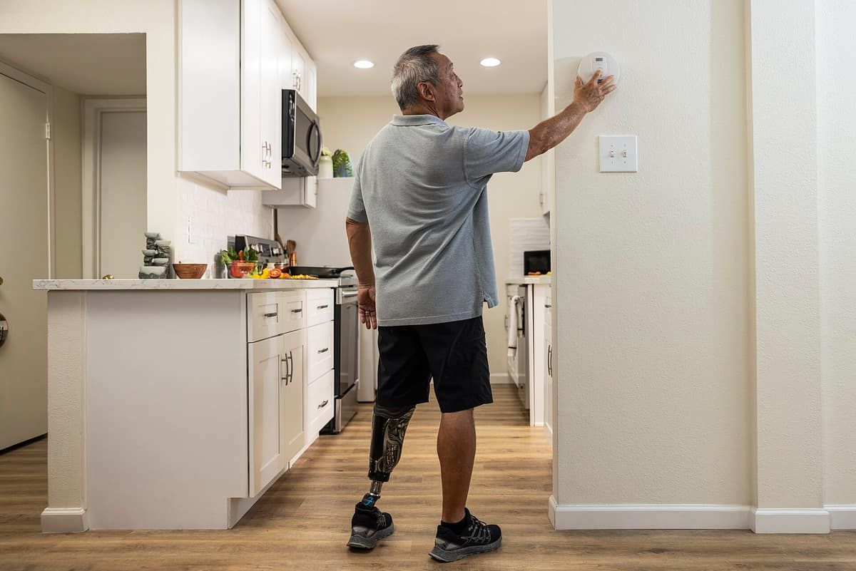 A man in a kitchen reaching up to press the test button on a ceiling smoke alarm