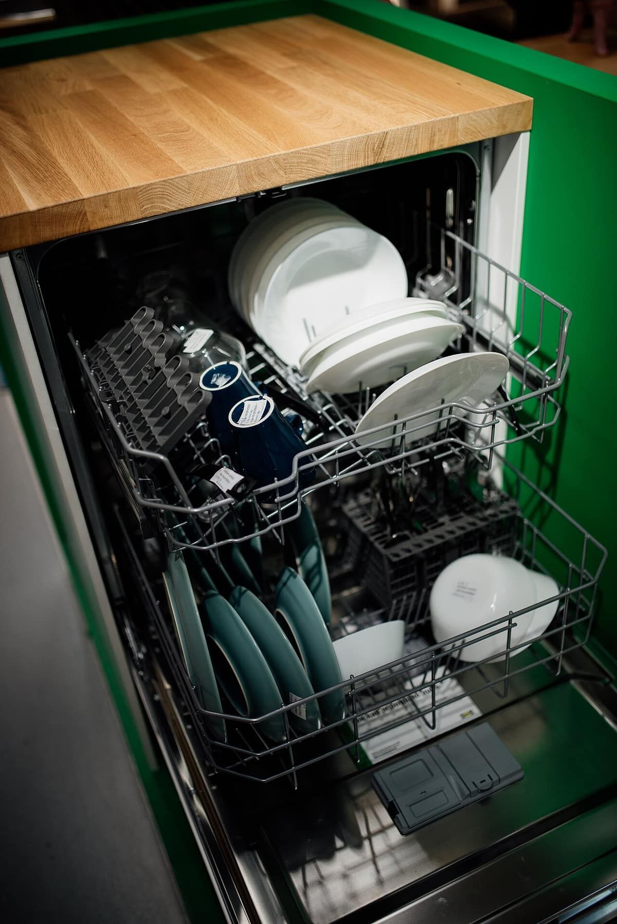 A dishwasher with its door open and racks loaded with plates and glasses