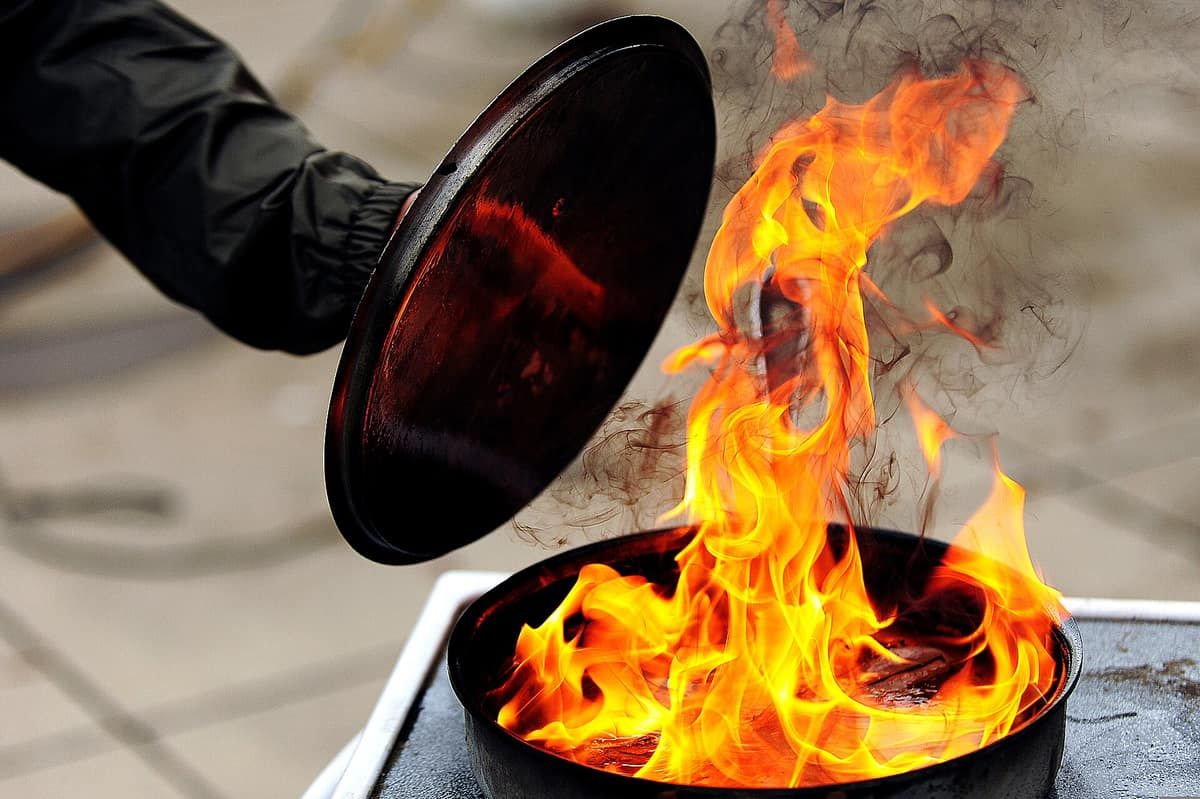 A person lowering a lid onto a pot of burning oil during a fire-safety demonstration
