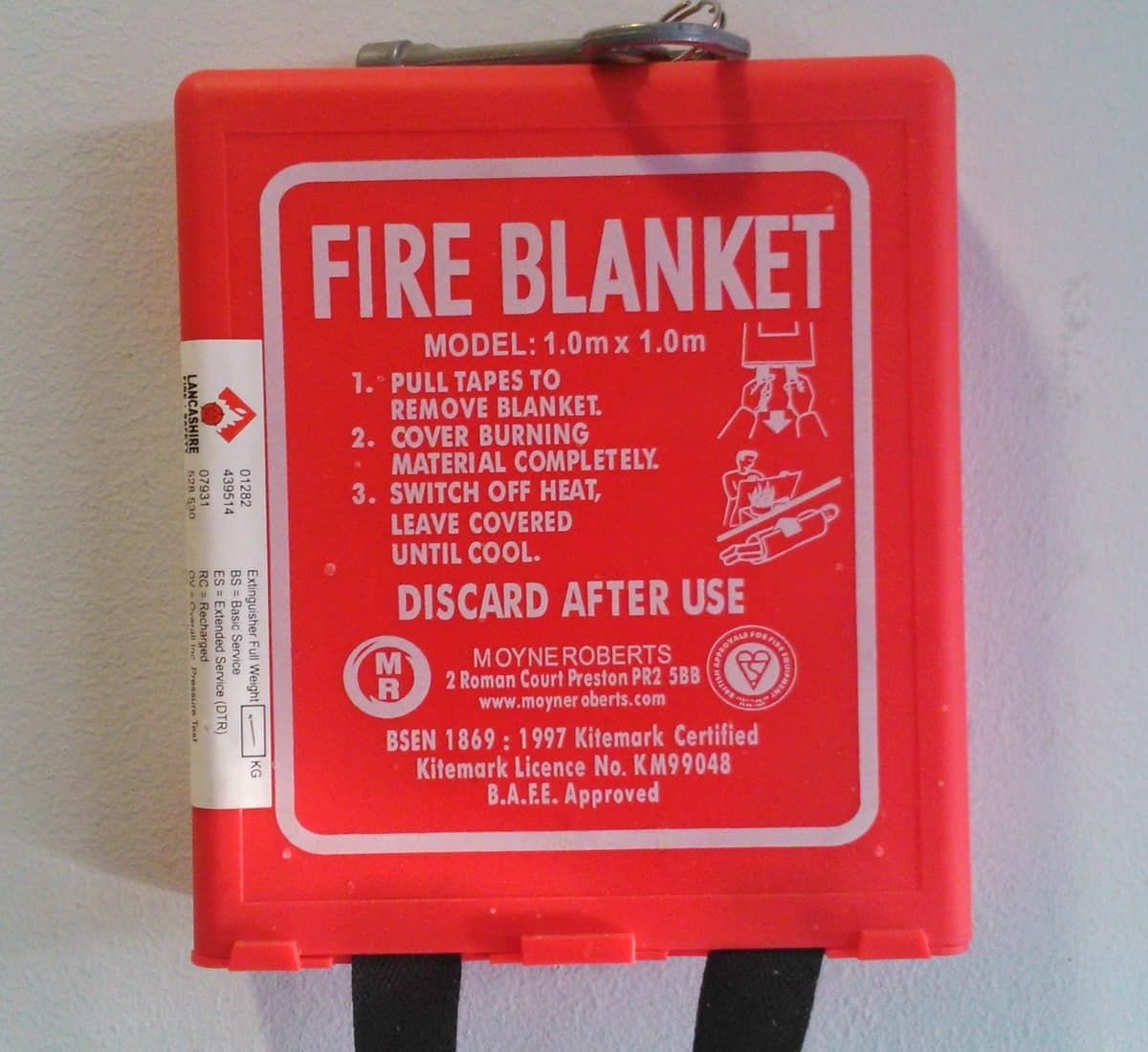 A red kitchen fire blanket in its wall pouch with printed instructions