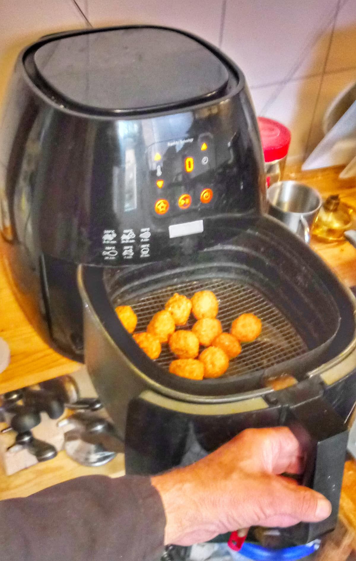 A hand pulling out an air fryer basket filled with falafel
