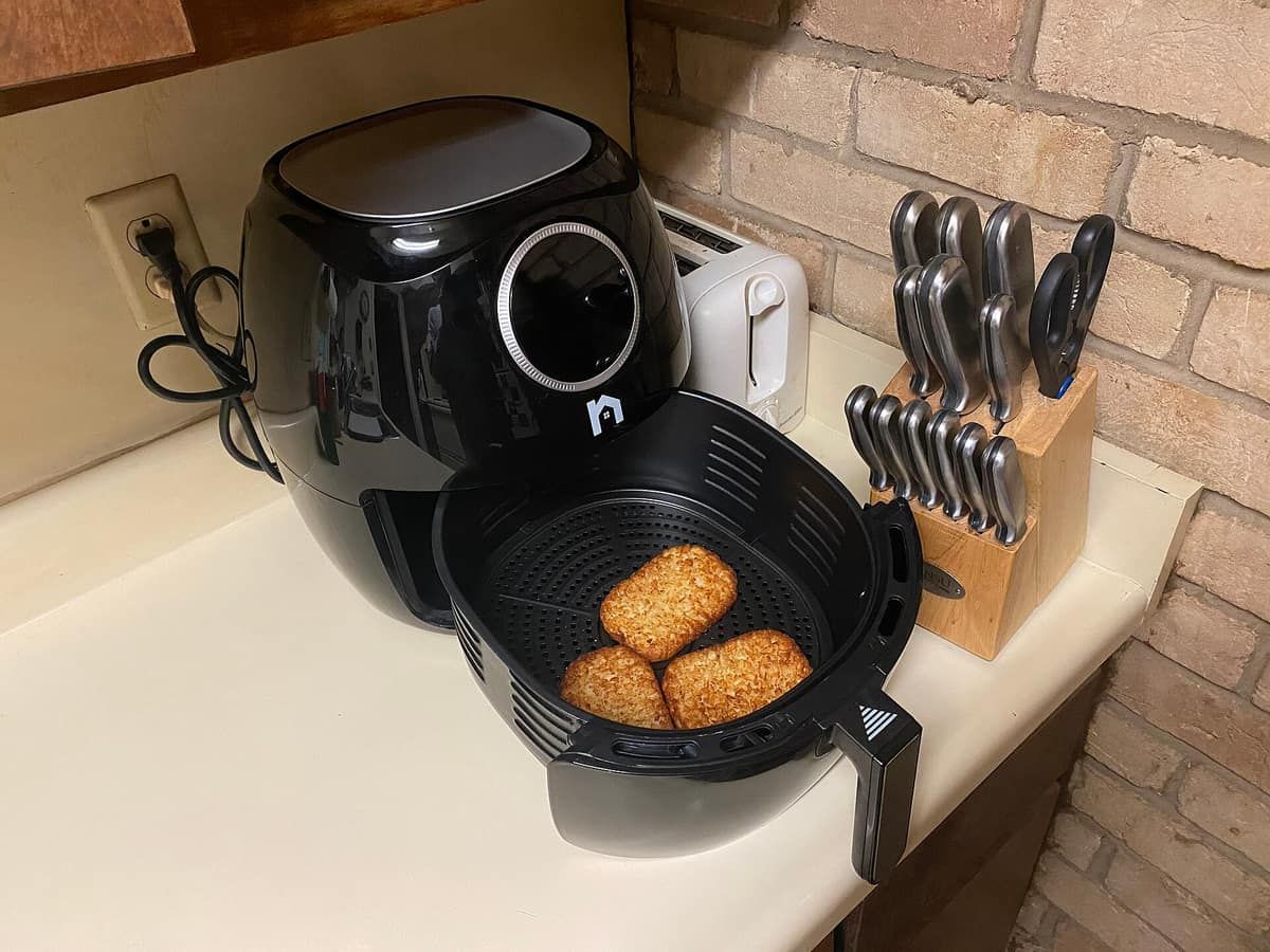 A black basket air fryer on a kitchen counter with its drawer open and two breaded fillets inside