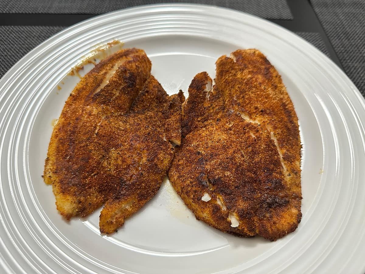 Two breaded tilapia fillets cooked in an air fryer, on a white plate