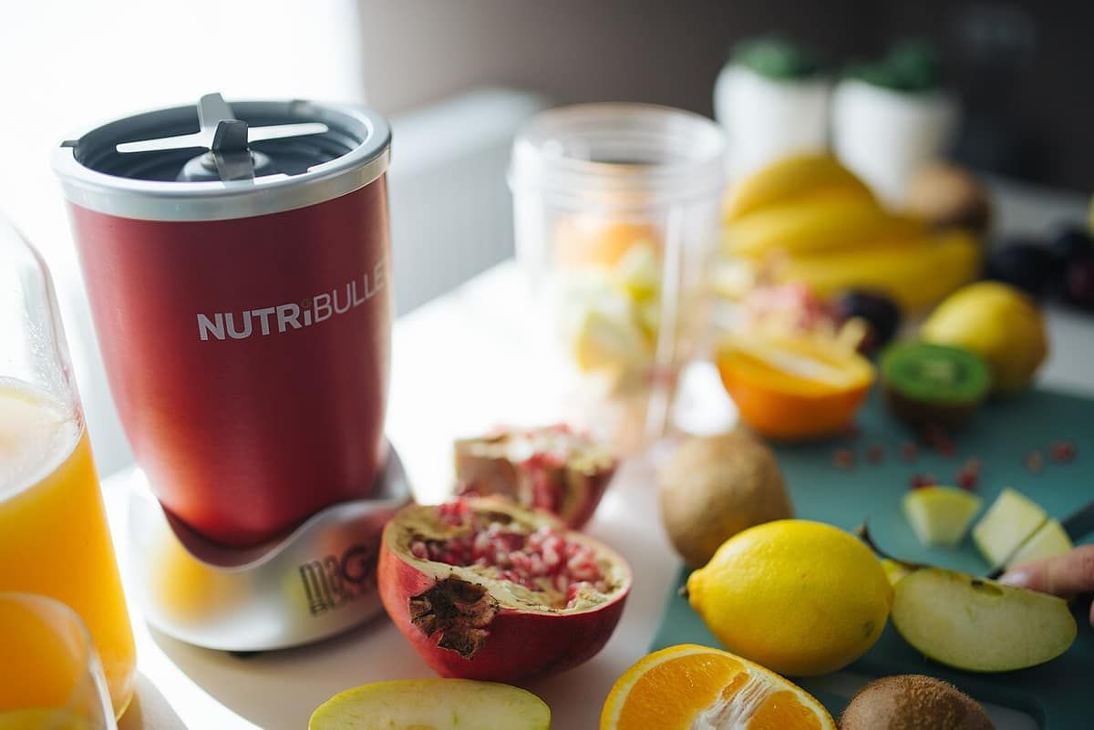 A red NutriBullet personal blender on a counter surrounded by cut fruit