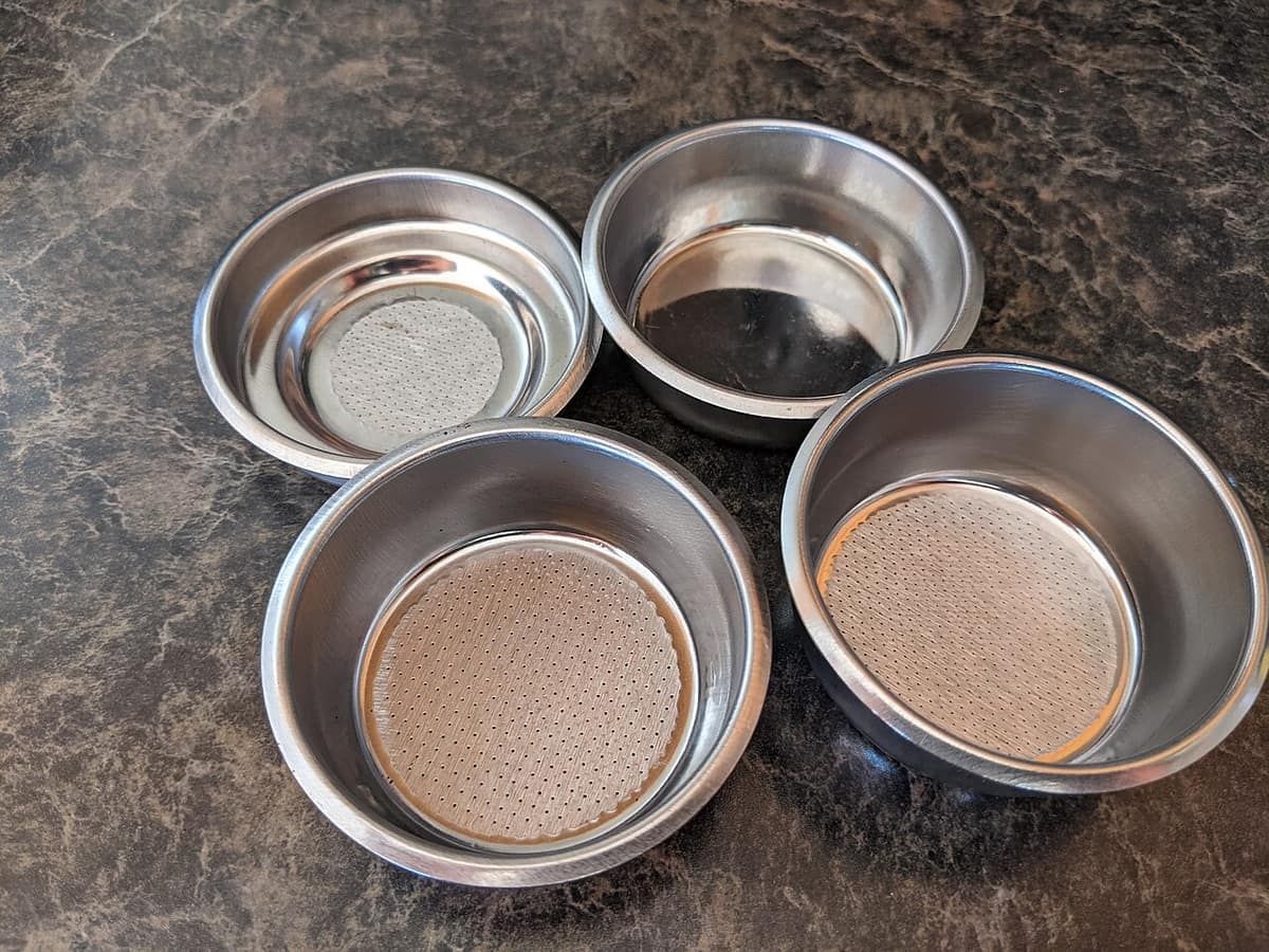 Five stainless espresso filter baskets of different sizes laid out on a countertop