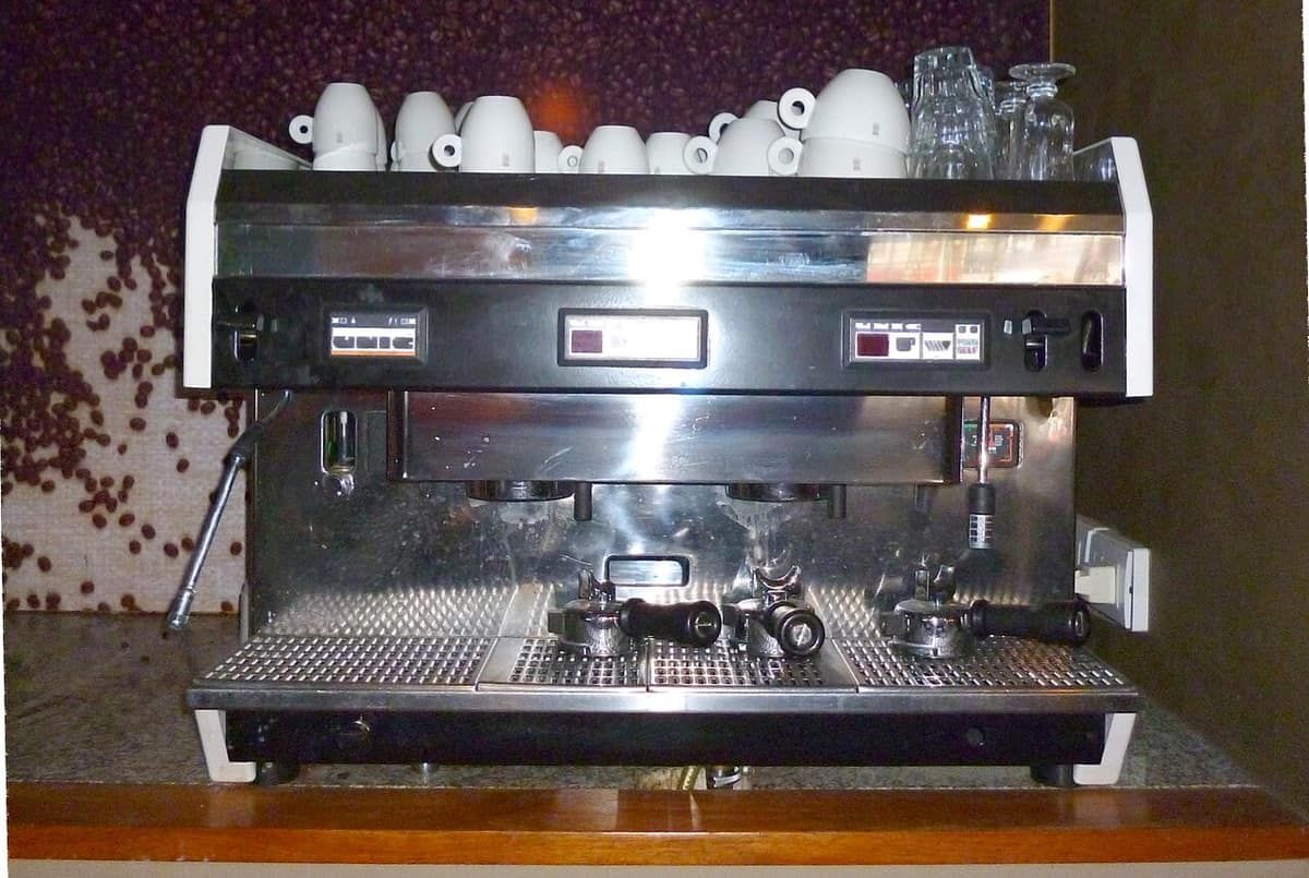 A large multi-group commercial espresso machine on a café counter, with cups stacked on top