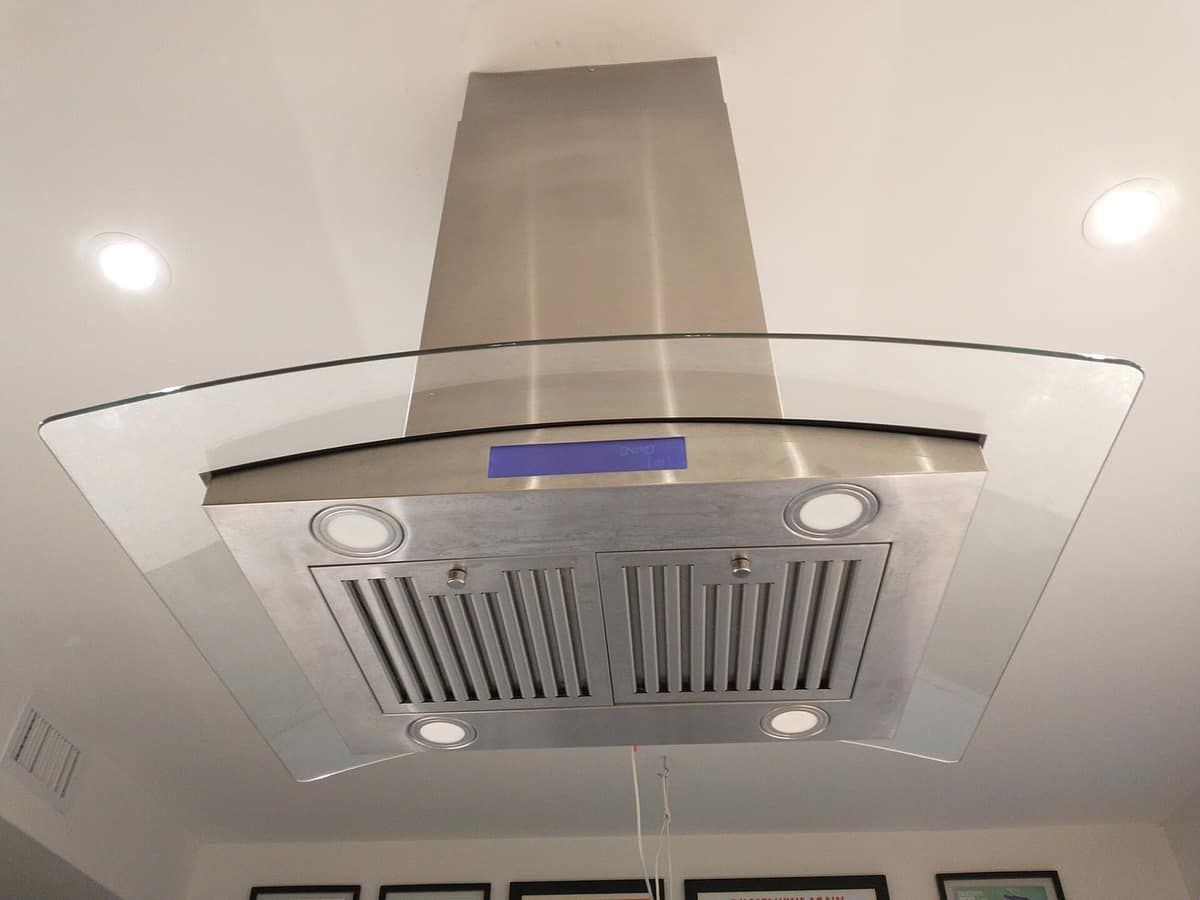 Stainless steel and glass range hood mounted above a kitchen island cooktop