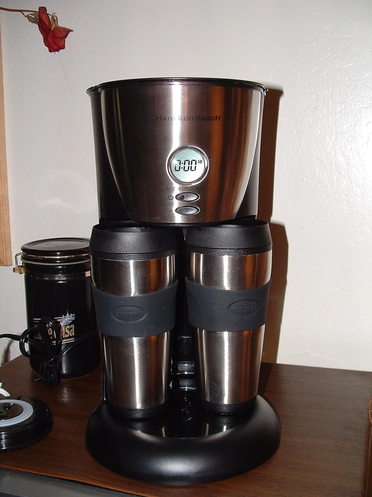 A black and stainless drip coffee maker brewing into two insulated travel mugs