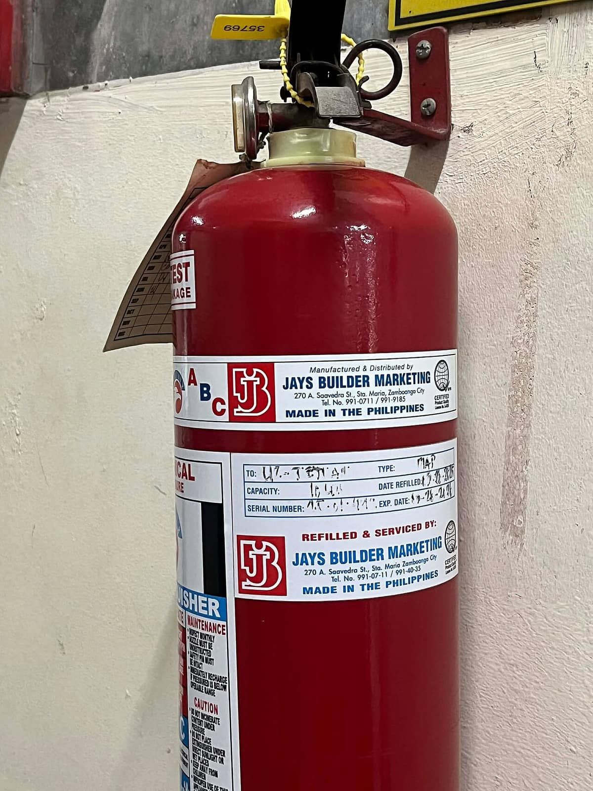 A red ABC-rated fire extinguisher hanging on a wall, with its pressure gauge and tamper seal visible at the top